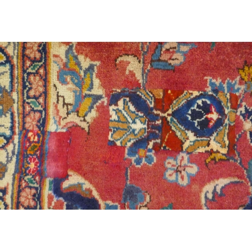 1020 - A washed red ground Persian Mashad carpet with traditional floral medallion design, signed by the we... 