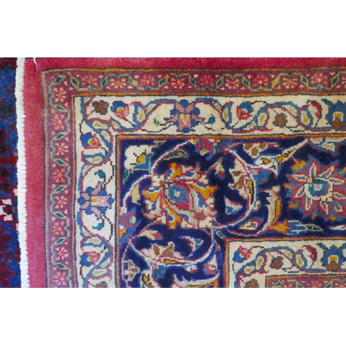 1020 - A washed red ground Persian Mashad carpet with traditional floral medallion design, signed by the we... 