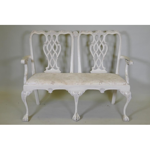 1029 - A painted Chippendale style two seater settee, with pierced back and carved decoration, raised on ca... 