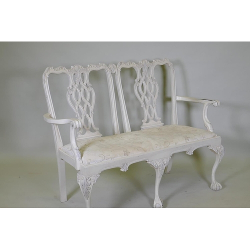 1029 - A painted Chippendale style two seater settee, with pierced back and carved decoration, raised on ca... 