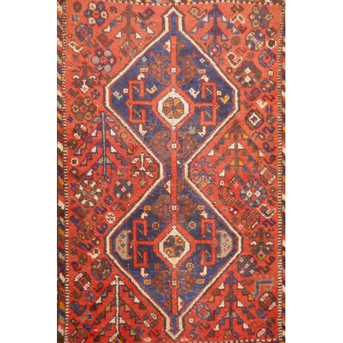 1040 - An antique Persian wool rug, with twin blue ground medallions on a tomato field, 124 x 92cm