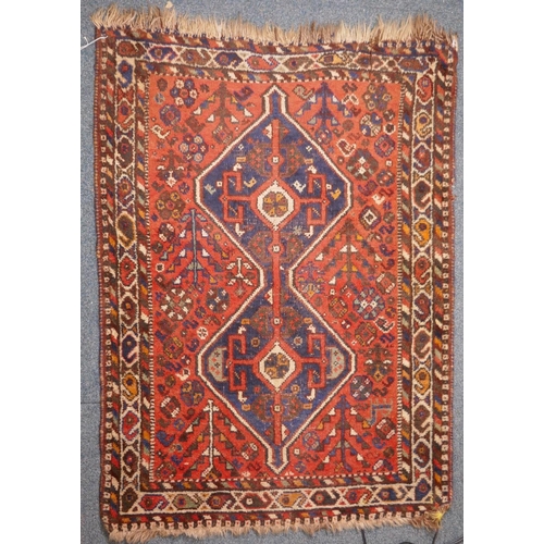 1040 - An antique Persian wool rug, with twin blue ground medallions on a tomato field, 124 x 92cm