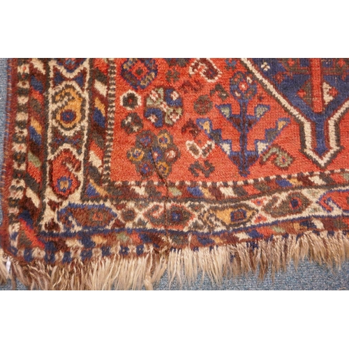 1040 - An antique Persian wool rug, with twin blue ground medallions on a tomato field, 124 x 92cm