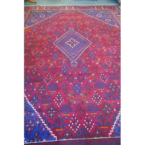 1060 - A claret and blue ground Persian Joshaghan tribal carpet with traditional medallion design, signed, ... 