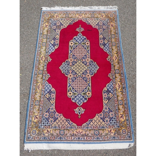 1064 - A full pile fine hand woven Iranian rug, signed and dated, with age, red ground with blue borders an... 