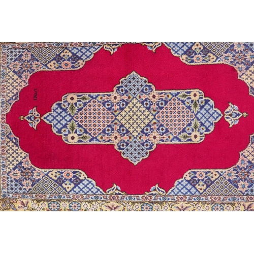 1064 - A full pile fine hand woven Iranian rug, signed and dated, with age, red ground with blue borders an... 