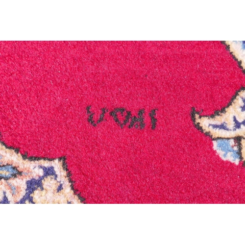 1064 - A full pile fine hand woven Iranian rug, signed and dated, with age, red ground with blue borders an... 