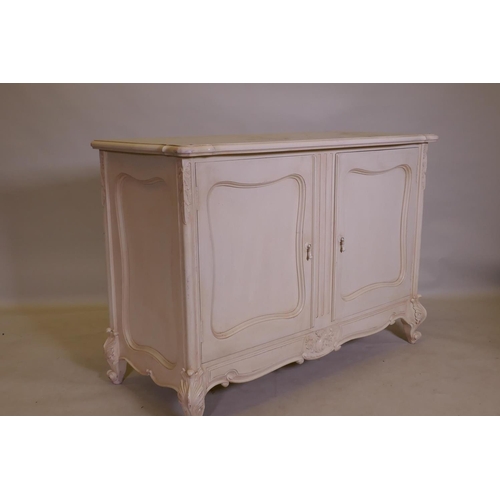 1094 - A French style painted buffet with shaped top and two cupboards, and carved decoration, raised on ca... 