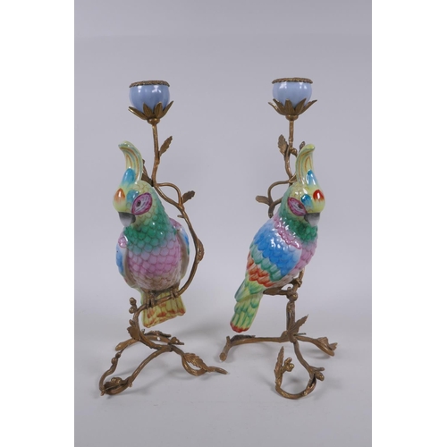 111 - A pair of gilt metal and porcelain candlesticks in the form of a brightly enamelled parrot perched o... 