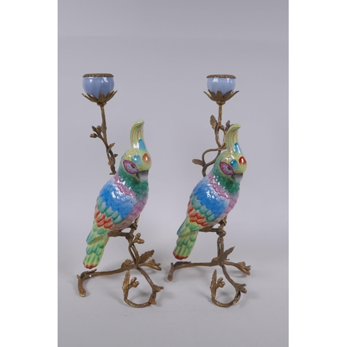 111 - A pair of gilt metal and porcelain candlesticks in the form of a brightly enamelled parrot perched o... 