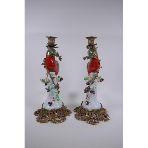 232 - A pair of polychrome porcelain and gilt mounted candle sticks in the form of a parrot perched on a s... 