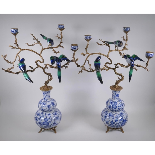 54 - A pair of polychrome porcelain and gilt metal three branch candlesticks, decorated with birds perche... 