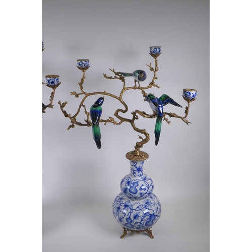 54 - A pair of polychrome porcelain and gilt metal three branch candlesticks, decorated with birds perche... 