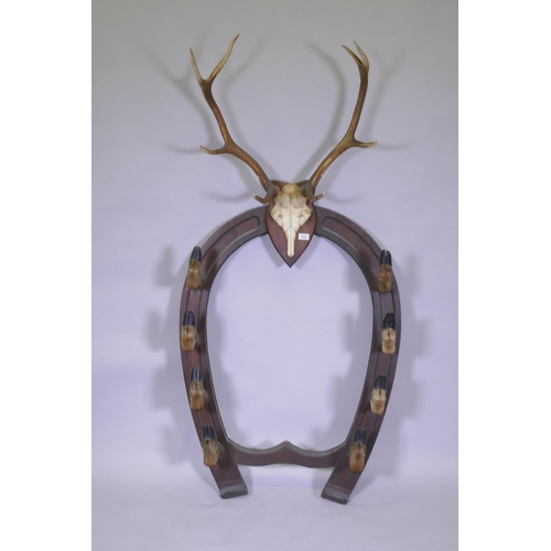 1022 - A Victorian oak gun rack in the form of horse shoe with deer's hoof hooks and antler crest, 84cm wid... 