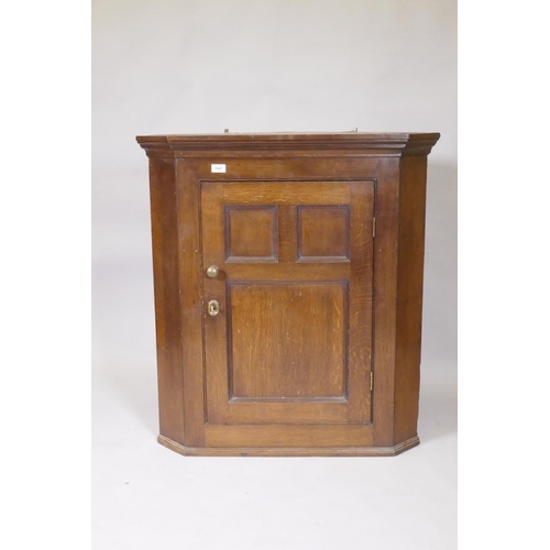 1047 - A Georgian oak hanging corner cupboard with three panelled door, original brass knob and escutcheon,... 