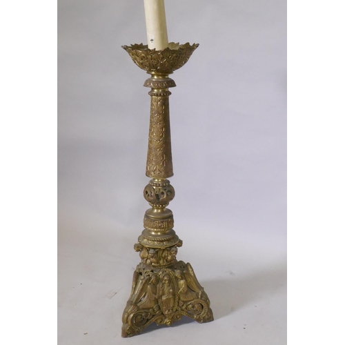 1056 - A gilt brass church torchere/pricket candlestick, decorated in relief with demons and angels, 144cm ... 