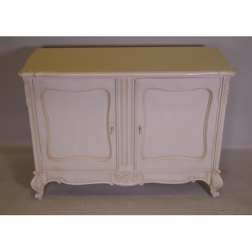 1111 - A French style painted buffet with shaped top and two cupboards, and carved decoration, raised on ca... 