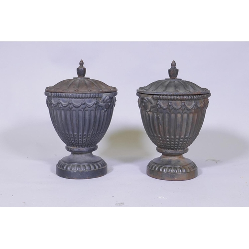 129 - A pair of antique cast iron fluted urns and covers with mask decoration, 30cm high