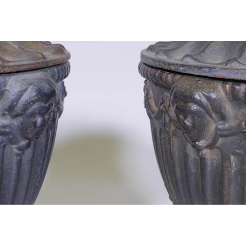 129 - A pair of antique cast iron fluted urns and covers with mask decoration, 30cm high