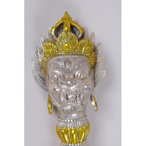 133 - A Tibetan white metal phurba, the handle decorated with the mask of a wrathful deity, 32cm long