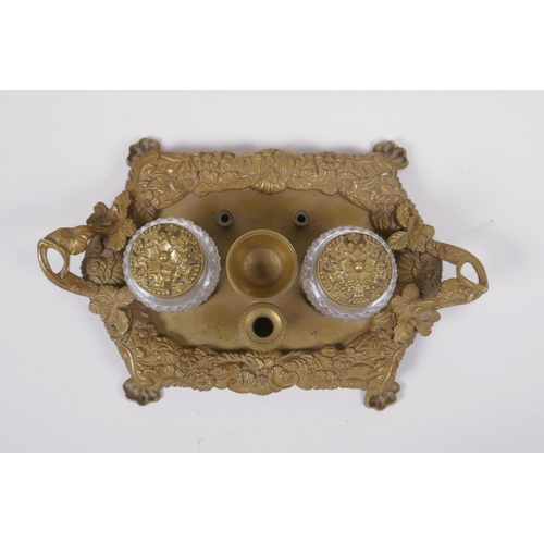 21 - An antique brass desk stand with raised vine decoration and two glass inkwells, 30 x 20cm