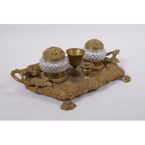 21 - An antique brass desk stand with raised vine decoration and two glass inkwells, 30 x 20cm