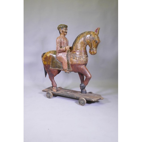 1025 - A carved and painted Indian figure of a mounted horseman, mounted on a base with wheels, 110cm high,... 