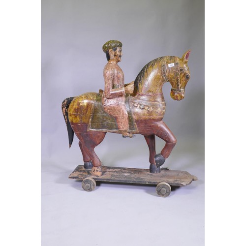 1025 - A carved and painted Indian figure of a mounted horseman, mounted on a base with wheels, 110cm high,... 