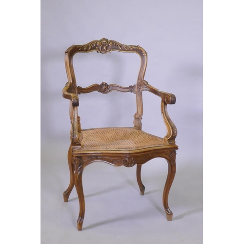 1022 - A C19th French carved walnut open arm chair with caned seat