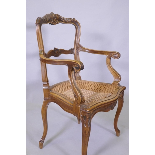 1022 - A C19th French carved walnut open arm chair with caned seat