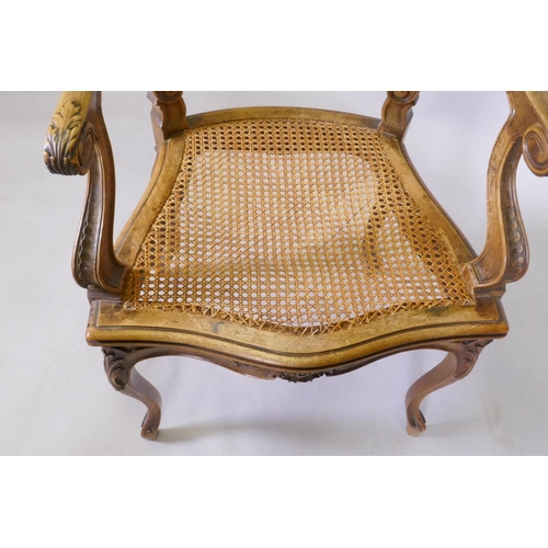 1022 - A C19th French carved walnut open arm chair with caned seat