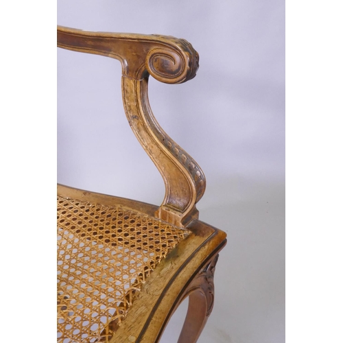 1022 - A C19th French carved walnut open arm chair with caned seat