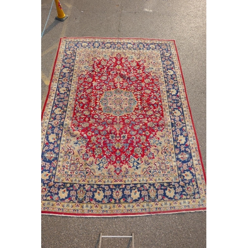 1091 - An Iranian red ground wool Isfahan carpet, with floral medallion design and blue borders, 275 x 375c... 