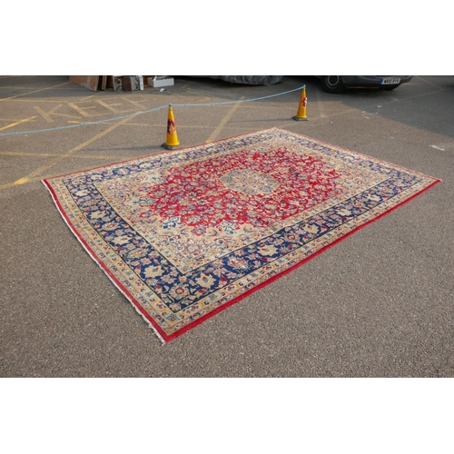 1091 - An Iranian red ground wool Isfahan carpet, with floral medallion design and blue borders, 275 x 375c... 