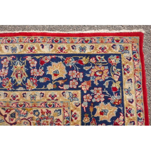 1091 - An Iranian red ground wool Isfahan carpet, with floral medallion design and blue borders, 275 x 375c... 