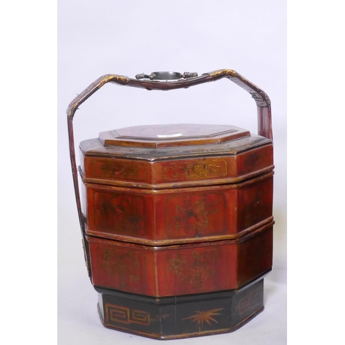 16 - A Chinese three section food container with lacquered decoration, plaited cane handle with metal mou... 