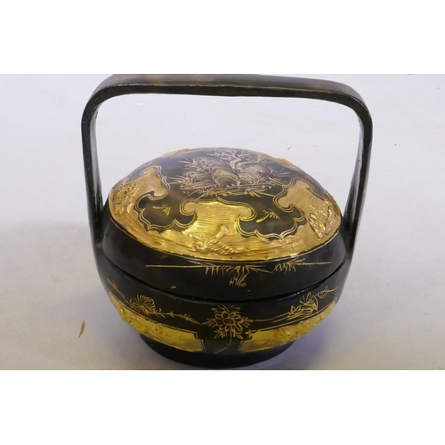 16 - A Chinese three section food container with lacquered decoration, plaited cane handle with metal mou... 