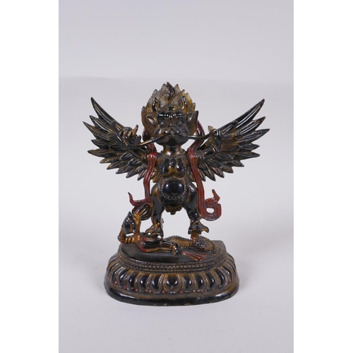 101 - A Tibetan lacquered and gilt bronze of Garuda standing on the back of a figure, 17cm high