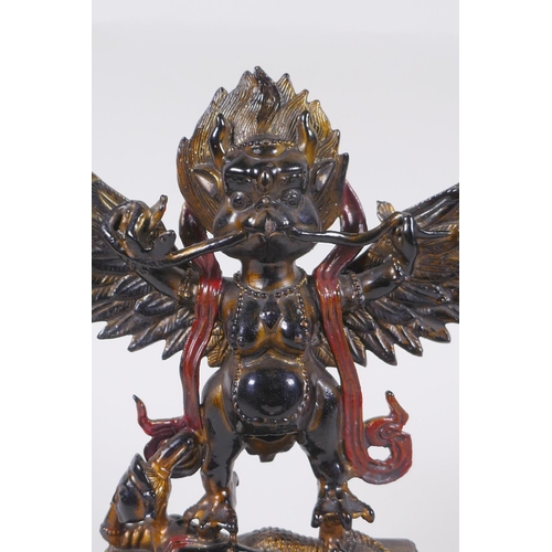 101 - A Tibetan lacquered and gilt bronze of Garuda standing on the back of a figure, 17cm high