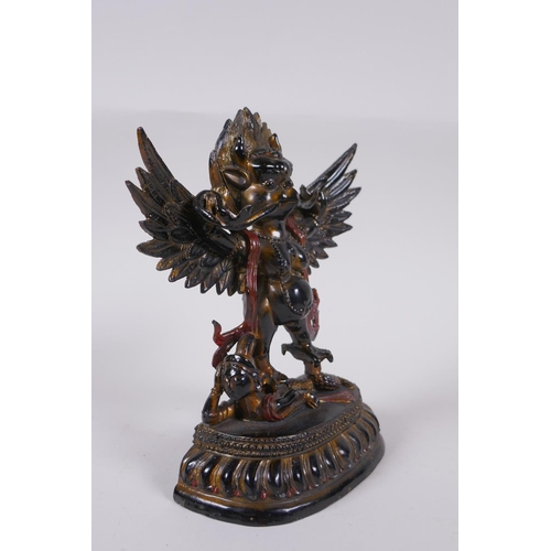 101 - A Tibetan lacquered and gilt bronze of Garuda standing on the back of a figure, 17cm high