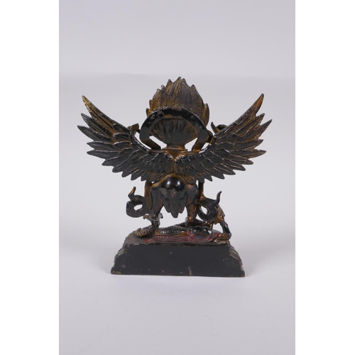 101 - A Tibetan lacquered and gilt bronze of Garuda standing on the back of a figure, 17cm high