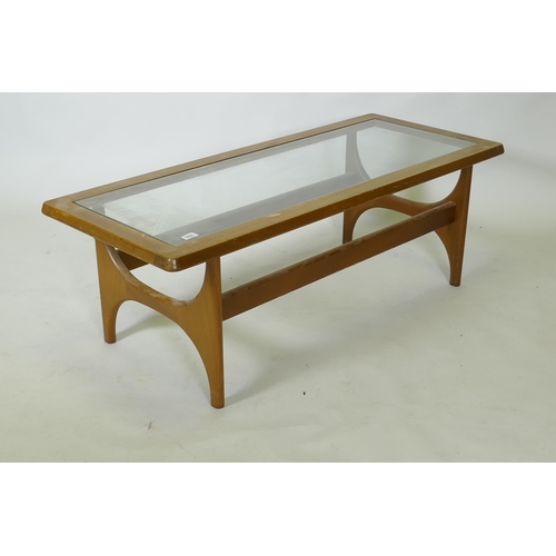 1058 - A mid century mahogany coffee table with inset glass top, raised on shaped end supports, bears label... 