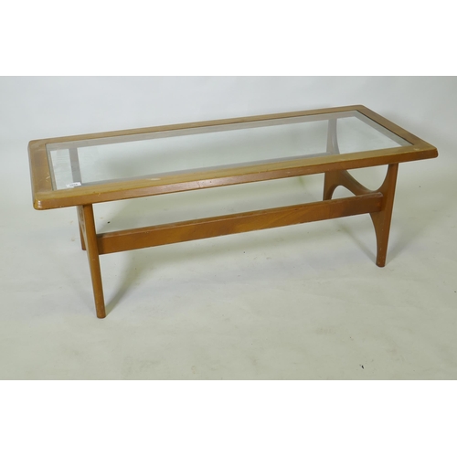 1058 - A mid century mahogany coffee table with inset glass top, raised on shaped end supports, bears label... 