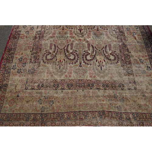 1072 - An antique Persian carpet with stylised flora and fauna designs on a faded gold field, with red bord... 