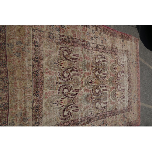 1072 - An antique Persian carpet with stylised flora and fauna designs on a faded gold field, with red bord... 