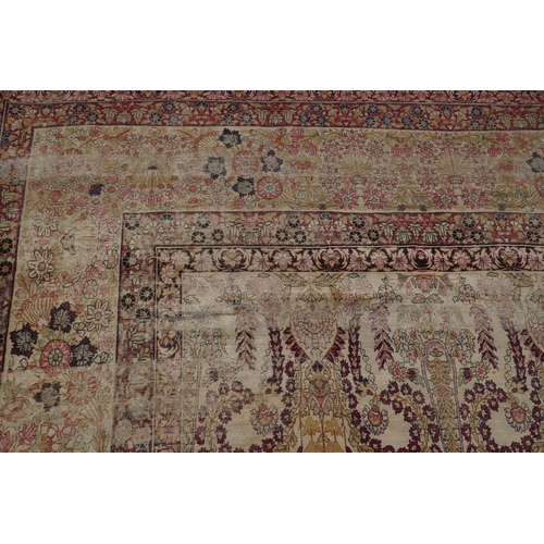 1072 - An antique Persian carpet with stylised flora and fauna designs on a faded gold field, with red bord... 