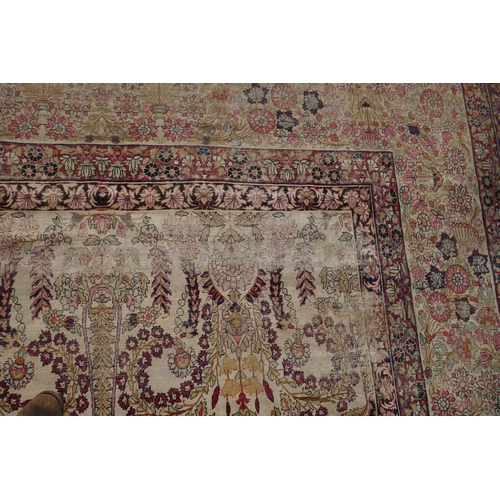 1072 - An antique Persian carpet with stylised flora and fauna designs on a faded gold field, with red bord... 