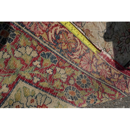 1072 - An antique Persian carpet with stylised flora and fauna designs on a faded gold field, with red bord... 