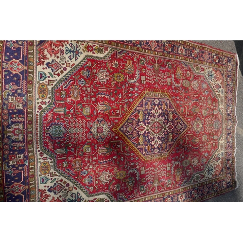 1075 - An antique Persian wool rug with medallion design on a red field with blue borders, 210 x 312cm