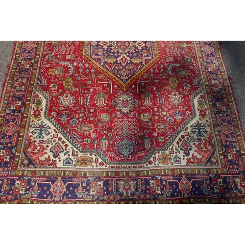 1075 - An antique Persian wool rug with medallion design on a red field with blue borders, 210 x 312cm